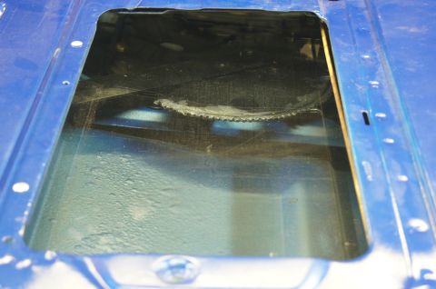 1979 Ford Bronco - Close-up of a blue painted metal panel with an opening, showing internal parts and a chain.
