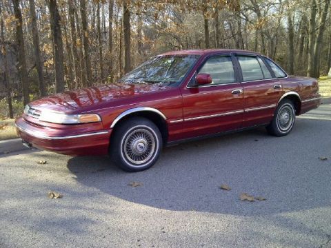 2000 Mercury Grand Marquis - A maroon sedan is parked on a paved surface, with a backdrop of trees.