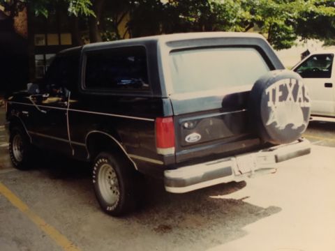 1993 Ford Bronco - A black Ford Bronco is parked next to another vehicle, with a Texas-themed spare tire cover.