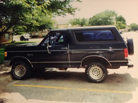 1993 Ford Bronco - Side view of a black Ford Bronco with tinted windows and a spare tire mounted on the back.