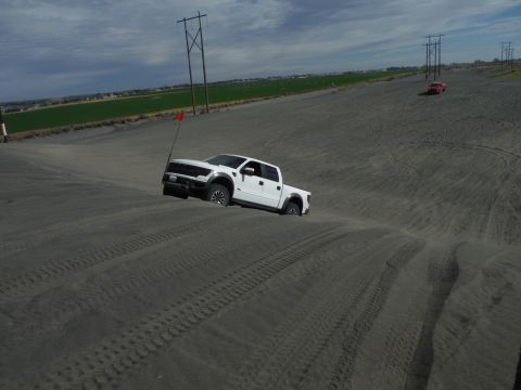 2005 Jeep Wrangler - White Ford Raptor pickup truck navigates sand dunes, with another vehicle visible in the background.
