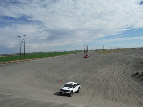 2005 Jeep Wrangler - Two trucks are driving on a sandy terrain under a cloudy sky with power lines in the background.