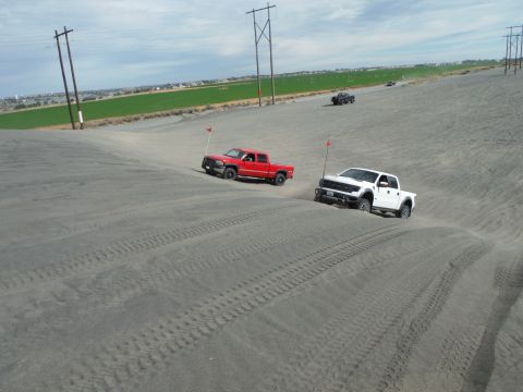 2005 Jeep Wrangler - Two pickup trucks navigate sandy terrain under a cloudy sky.