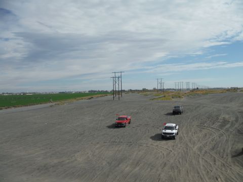 2005 Jeep Wrangler - Several trucks are driving across a dusty, open field under a cloudy sky, with power lines stretching into the distance.