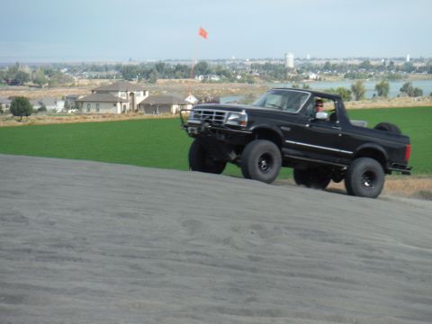 2005 Jeep Wrangler - Ford Bronco navigating a sand dune with a suburban landscape behind it.