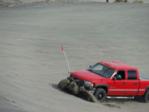 2005 Jeep Wrangler - A red pickup truck navigates through a sandy terrain, kicking up dirt.