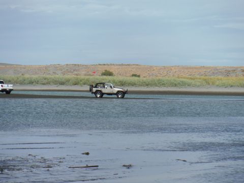 2005 Jeep Wrangler - A white Jeep Wrangler drives through shallow water near a sandy embankment under a cloudy sky.