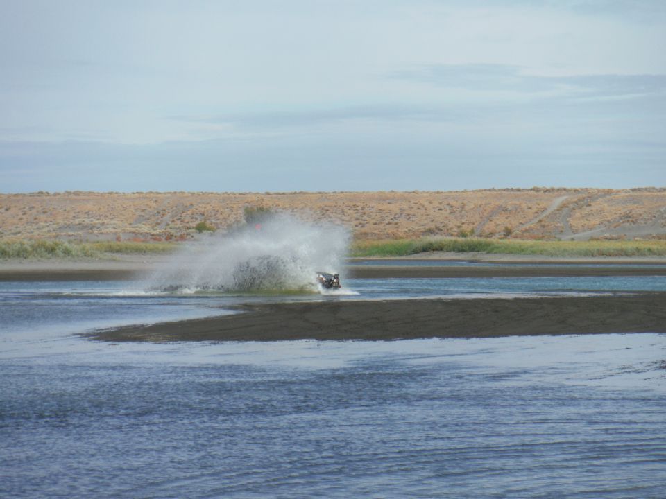 Off-road vehicle kicking up water on a sandy shore