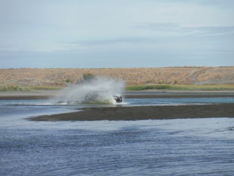2005 Jeep Wrangler - A black vehicle creates a large splash as it moves through the water near a sandy shore.