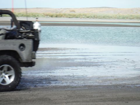 2005 Jeep Wrangler - A Jeep Wrangler drives along a sandy shore next to a body of water.