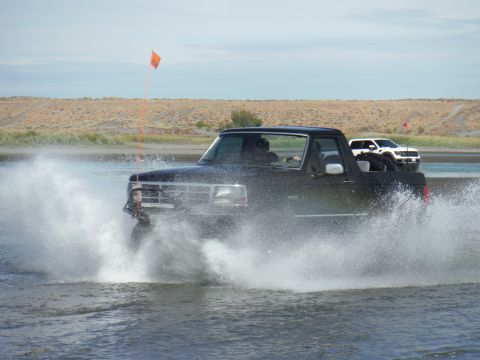 2005 Jeep Wrangler - A black pickup truck drives through the water, creating a large splash, with another vehicle visible in the distance.