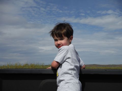 2005 Jeep Wrangler - A young child peers over the edge of a truck bed against a backdrop of a cloudy sky.