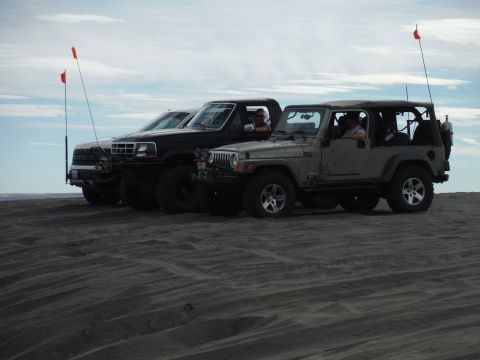 2005 Jeep Wrangler - A lineup of off-road vehicles, including a Jeep Wrangler, parked on a sandy terrain with red flags on poles.