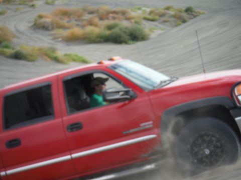 2005 Jeep Wrangler - A red pickup truck navigates a sandy landscape, with dust billowing around its wheels.