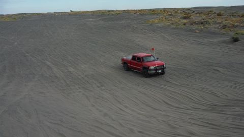 2005 Jeep Wrangler - A red pickup truck navigates sandy terrain, kicking up dust as it drives across the dunes.