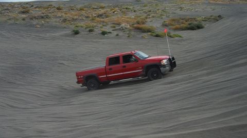2005 Jeep Wrangler - Red pickup truck navigates sandy terrain with a flag on an antenna.