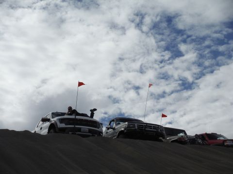 2005 Jeep Wrangler - Multiple vehicles are parked on a sand dune with red flags marking their locations against a cloudy sky.