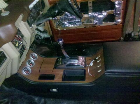 1982 Ford Bronco - The interior of a vehicle shows a custom center console with a chrome shifter, wood grain trim, and three gauges. The dashboard and steerin…