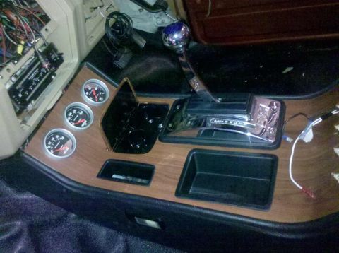 1982 Ford Bronco - A close-up interior shot shows a custom wood grain dash panel with three gauges and a chrome automatic shifter in a vehicle that appears to…