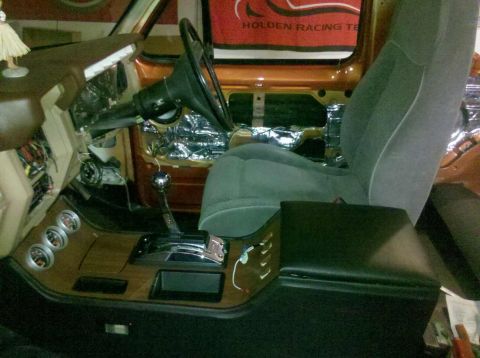1982 Ford Bronco - The interior of a vehicle is shown, featuring a steering wheel, dashboard, automatic gear shifter, and a bucket seat. The dashboard has woo…
