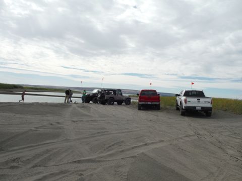2005 Jeep Wrangler - A group of people stand near a body of water next to a dark colored Jeep Wrangler and a red pickup truck. A white pickup truck is parked fu…