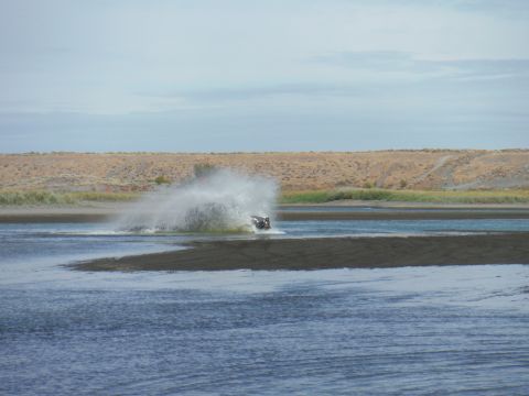 2005 Jeep Wrangler - A black and white personal watercraft is kicking up a large spray of water as it maneuvers in a shallow body of water. The background shows…