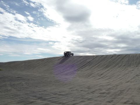 2005 Jeep Wrangler - A Jeep Wrangler drives over a sand dune under a cloudy sky. The sand dune has distinct ripple patterns from the wind.