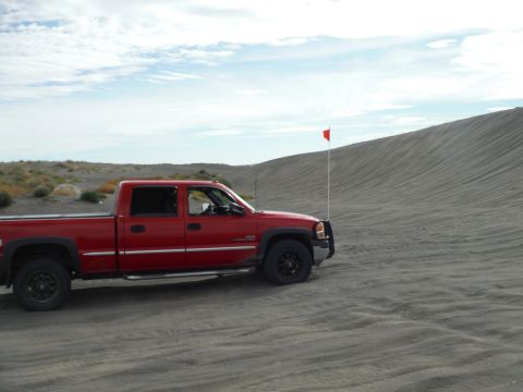 2005 Jeep Wrangler - A red pickup truck is parked on a sandy dune with a red flag mounted on the front. The truck is angled to the right, showcasing its side pr…