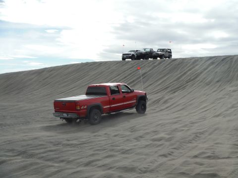 2005 Jeep Wrangler - A red pickup truck drives up a sand dune with other vehicles parked on the crest of the dune in the background. The truck has a tonneau cov…