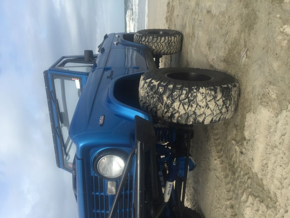 Blue Ford Bronco on a sandy beach with large off-road tires.
