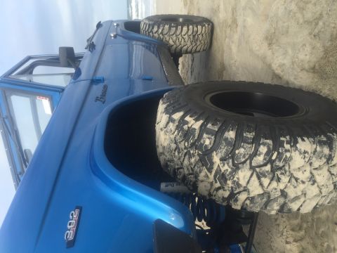 1974 Ford Bronco - A bright blue Ford Bronco is parked on a sandy beach with the ocean in the background. The vehicle has large, aggressive off-road tires cov…