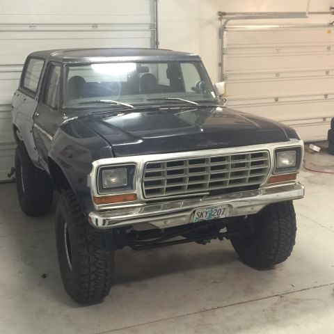 1979 Ford Bronco - A dark blue 1979 Ford Bronco is parked inside a garage, facing the camera. The vehicle has a chrome grille and bumper, and off-road tires.