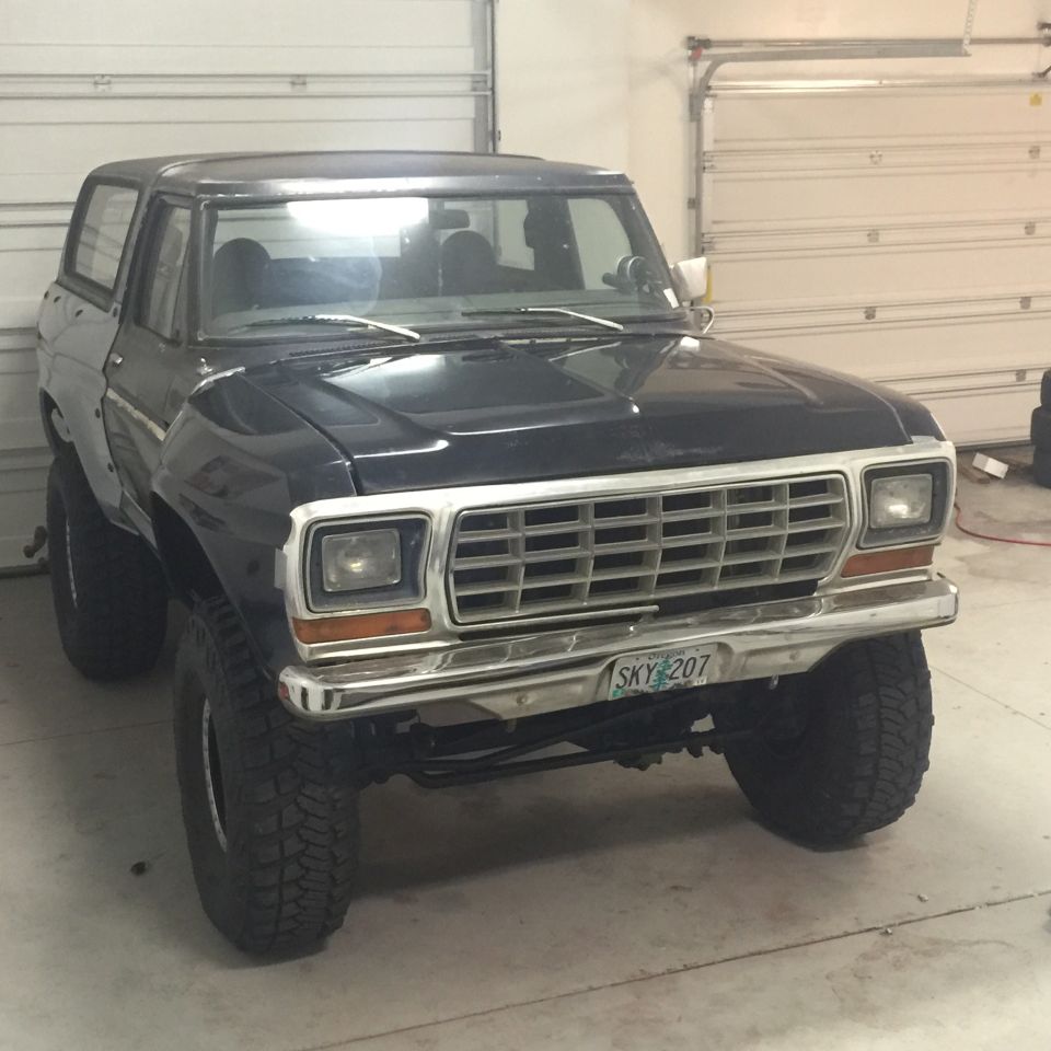 1979 Ford Bronco in a garage, front view, dark blue, chrome grille, off-road tires