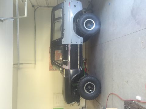 1979 Ford Bronco - A lifted, two-tone black and grey SUV is parked in a garage. The vehicle has large off-road tires and appears to be undergoing modification…