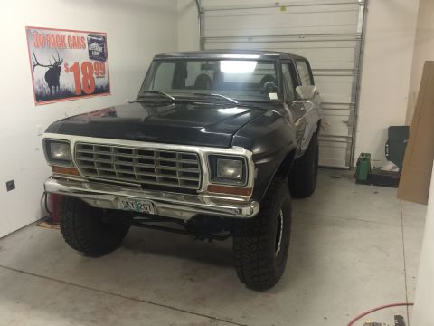 1979 Ford Bronco - A dark blue 1979 Ford Bronco is parked in a garage with a large overhead door in the background. A sign advertising "30 PACK CANS" for $18.…