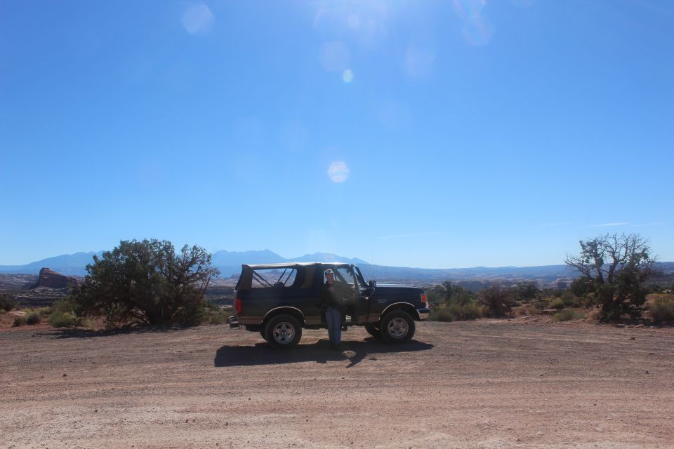 Person standing next to a dark blue Ford Bronco with removable top in a desert landscape.