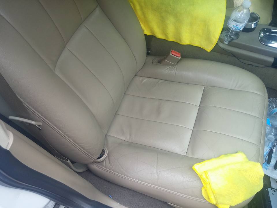 Car interior showing tan leather seats, a yellow towel, and a water bottle on the center console