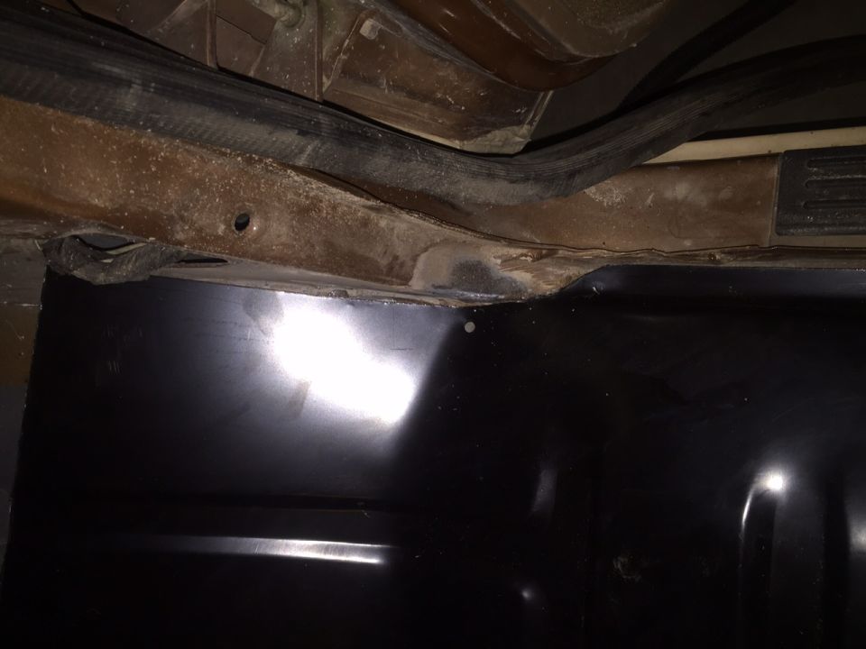 Underside of a vehicle showing a new black fuel tank and rusty frame.