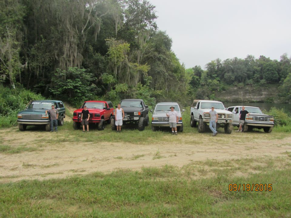 Six Ford trucks and SUVs parked in a line with five men standing next to them.