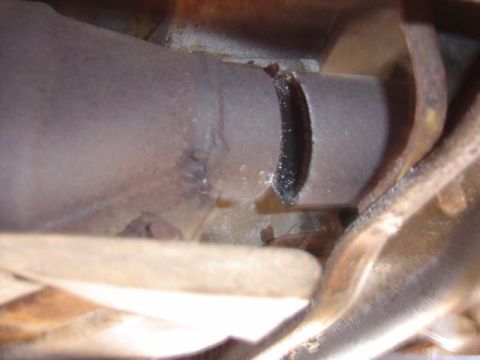 1986 Ford Bronco - A close-up view shows a hole cut into an exhaust pipe, likely for a header installation.