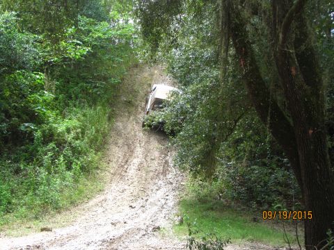 1995 Ford Bronco - A white SUV is stuck on a steep, muddy incline surrounded by dense green foliage. The vehicle appears to be a 1995 Ford Bronco.