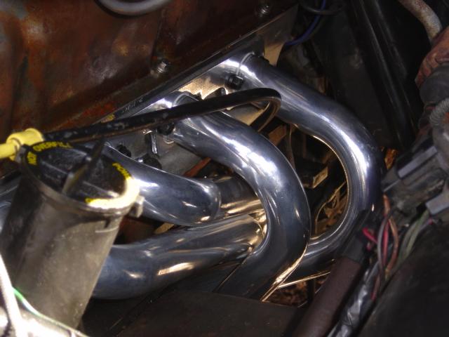 Chrome exhaust headers installed in an engine bay with black wiring routed over the tubes
