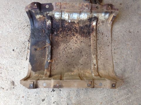 1979 Ford Bronco - This is a close-up, overhead view of a heavily rusted and dirty metal undercarriage part, possibly a skid plate, with visible oil and debri…