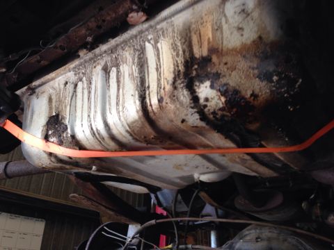 1979 Ford Bronco - Underside view of a vehicle's fuel tank, which appears to be heavily corroded and stained. An orange strap is wrapped around the tank.