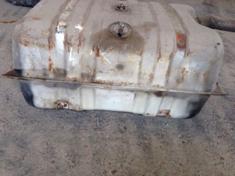 1979 Ford Bronco - A rusty, silver metal fuel tank is shown from a side angle, resting on a concrete surface. The tank has visible seams, mounting straps, and…
