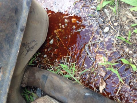 1979 Ford Bronco - A close-up view shows a rusty exhaust pipe leaking a dark, viscous fluid onto the ground next to a large metal object. The fluid appears to…