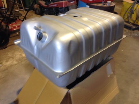 1979 Ford Bronco - A silver metal fuel tank is shown from a 3/4 front angle, resting on a cardboard box in a garage setting. The tank has a ribbed top and a c…