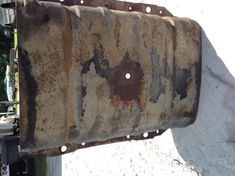 1979 Ford Bronco - A heavily rusted and weathered oil pan is shown in detail, resting on a light-colored surface. The pan exhibits significant peeling paint a…