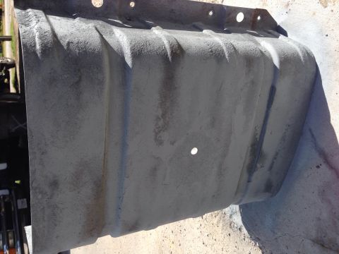 1979 Ford Bronco - A gray, metal fuel tank with visible ridges and mounting holes is shown from a side angle, resting on a concrete surface.