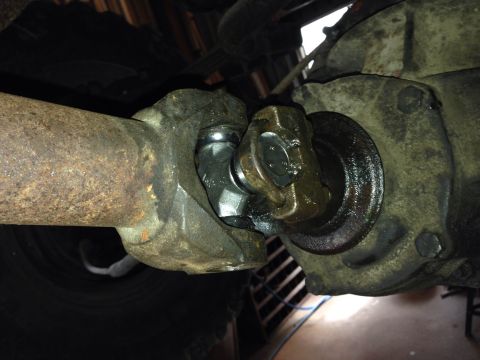 1979 Ford Bronco - A close-up view of a U-joint connecting a rusty driveshaft to a differential housing on a vehicle. The U-joint appears to be new and grease…